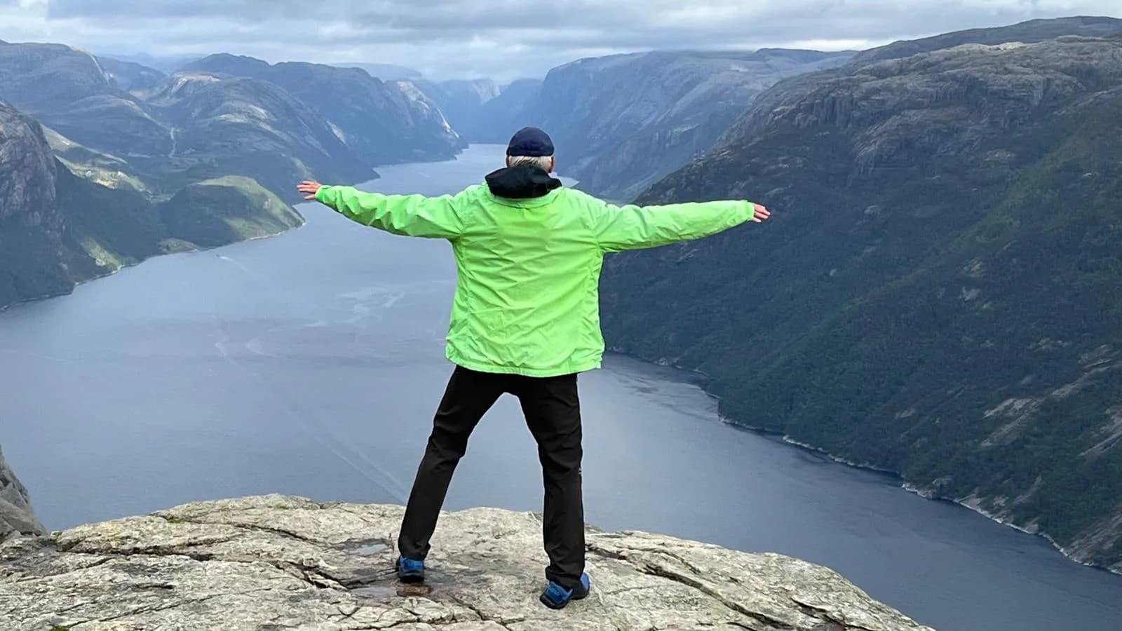 Turista s rozpaženými rukami nad Lysefjordom pri výstupe na Preikestolen v Nórsku