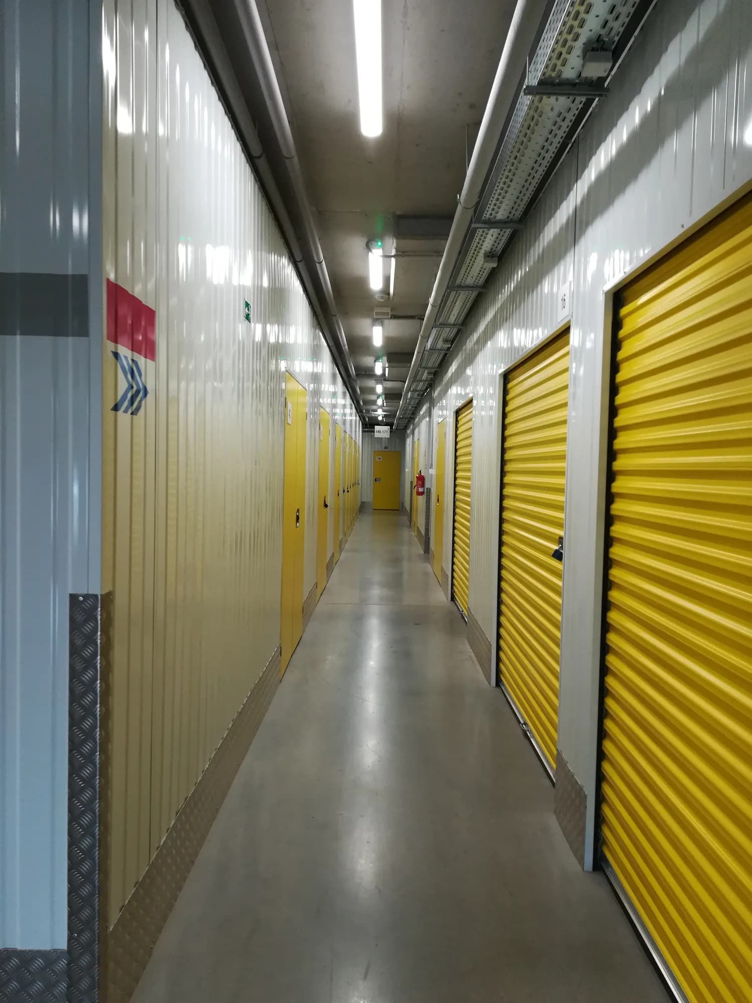 Dlhá chodba skladu so žltými rolovacími dverami boxov a bielymi stenami