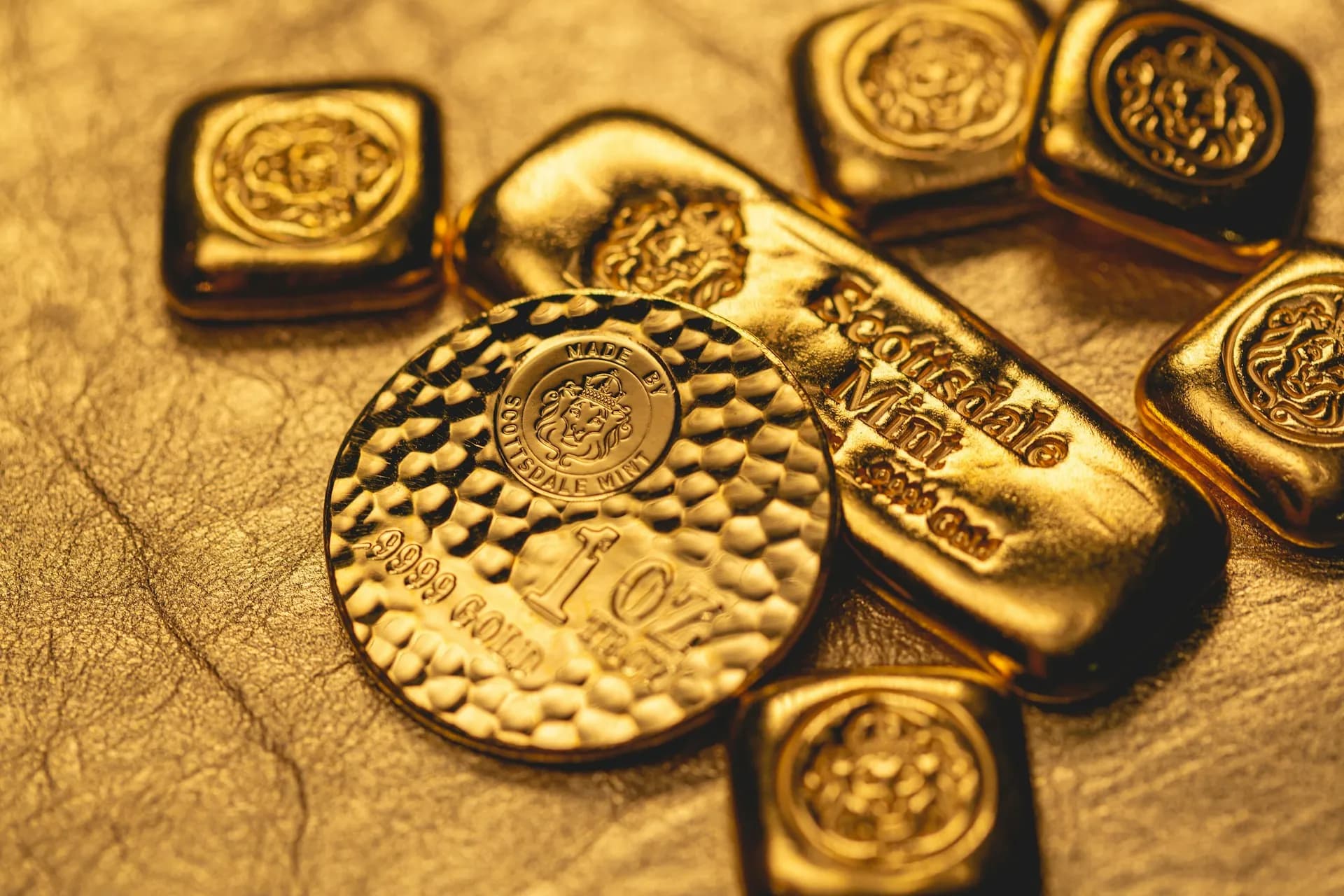 Zlatá minca s kladivkovým vzorom 1 oz a označením .9999 Gold od Scottsdale Mint medzi zlatými tehličkami s lvom (about 110 characters)