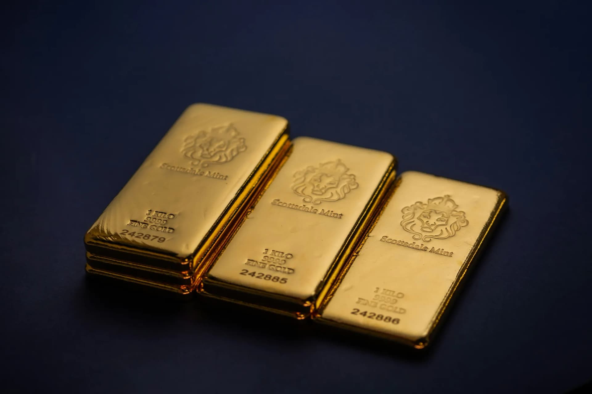Tri zlaté tehly Scottsdale Mint po 1 kilo s označením 9999 fine gold na tmavomodrom pozadí